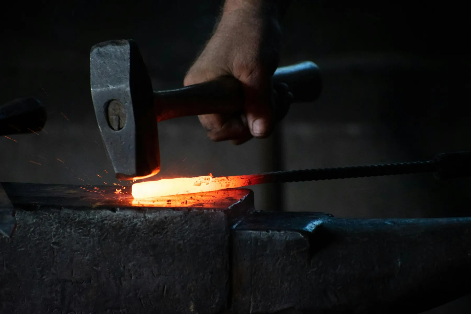 Blacksmith hammering a red-hot iron bar on an anvil